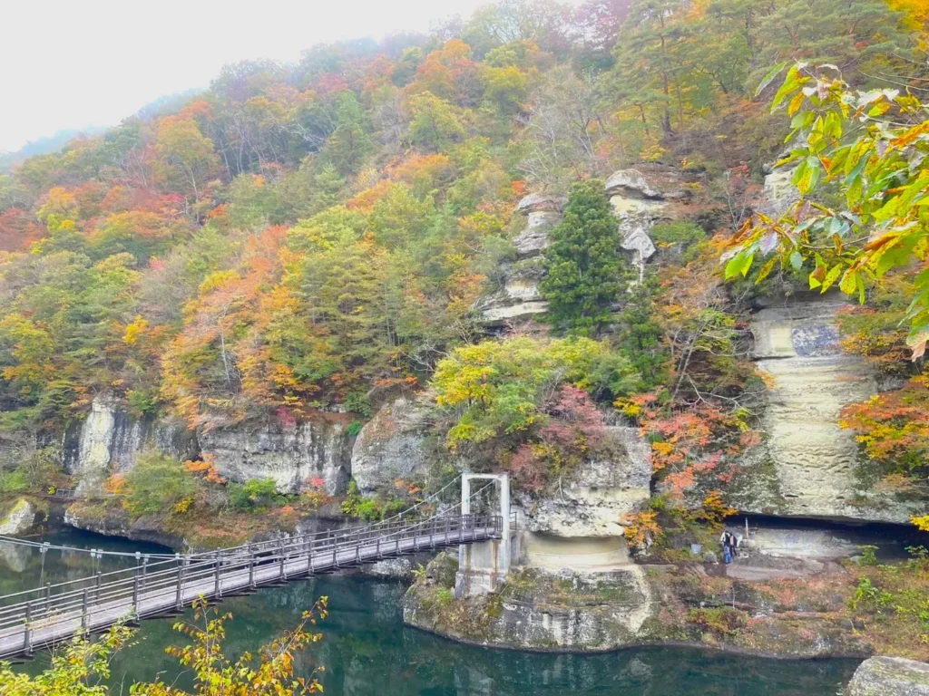 紅葉に染まり、塔のように突き出た岩にかかる吊り橋