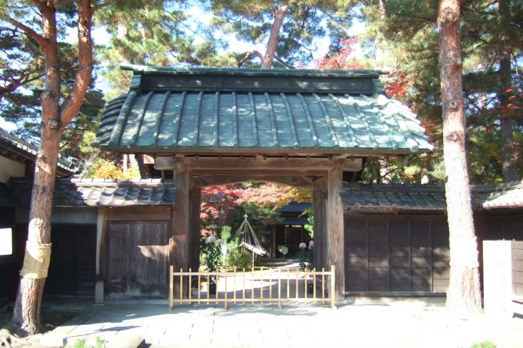 歴史的な屋敷の門から奥の紅葉が見える様子。
