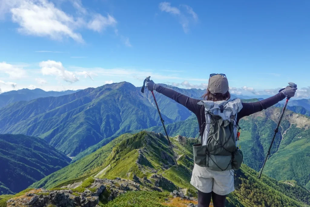 緑の絨毯に覆われた山の頂上で、女性の登山者が大きくてを広げている様子